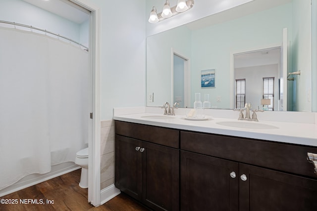 full bath with double vanity, a sink, toilet, and wood finished floors