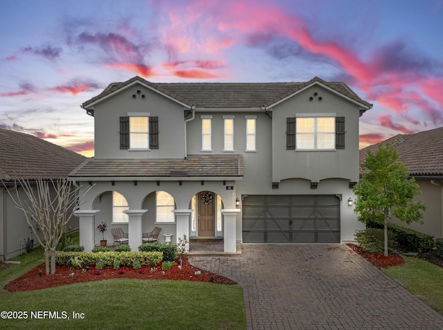 view of front facade featuring a garage, a tile roof, decorative driveway, a yard, and stucco siding