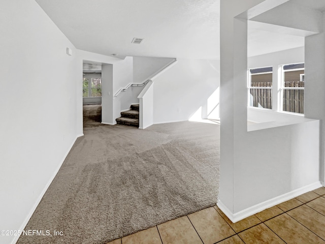 unfurnished living room with light carpet, visible vents, baseboards, stairway, and light tile patterned flooring