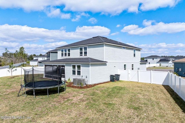 back of house featuring a trampoline, a fenced backyard, and a lawn