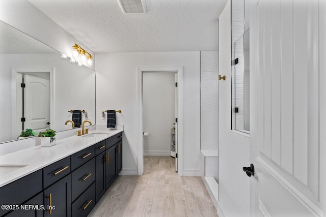 bathroom featuring visible vents, a sink, a textured ceiling, wood finished floors, and tiled shower