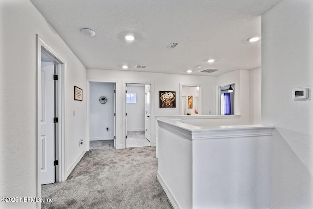 hall with carpet, visible vents, a textured ceiling, and baseboards