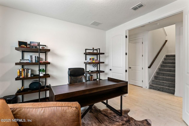 office area with a textured ceiling, visible vents, and light wood-style floors