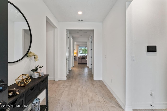 hallway featuring visible vents, light wood-style flooring, and baseboards