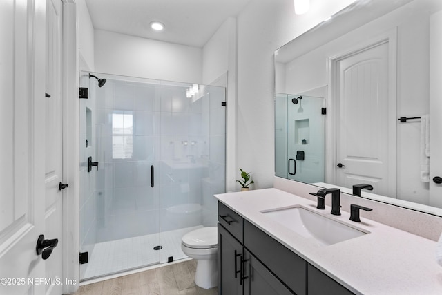 bathroom featuring toilet, a shower stall, wood finished floors, and vanity