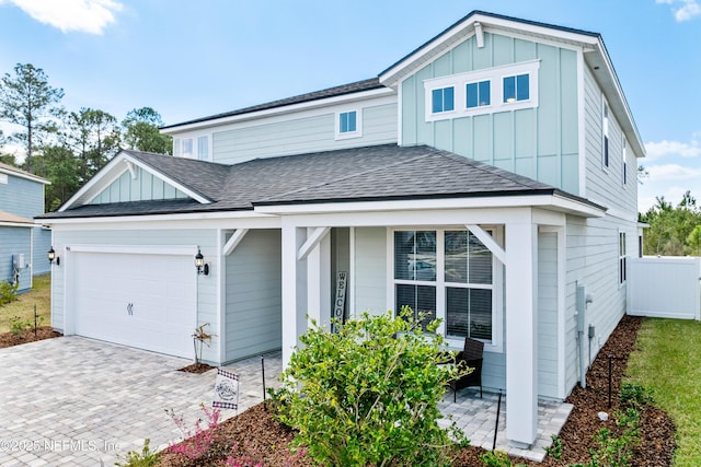 view of front of home with decorative driveway, roof with shingles, an attached garage, board and batten siding, and fence