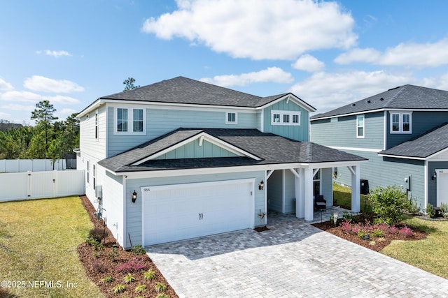 traditional-style home with an attached garage, fence, decorative driveway, board and batten siding, and a front yard