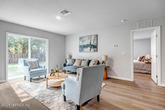 living room with a textured ceiling, light wood-type flooring, and visible vents