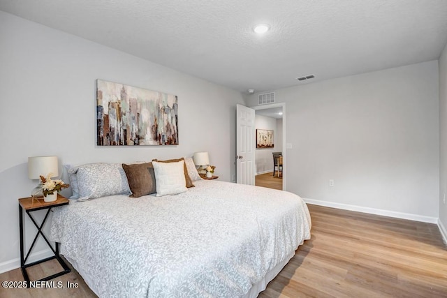 bedroom with visible vents, a textured ceiling, baseboards, and wood finished floors