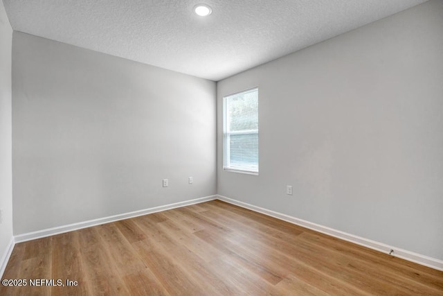 spare room with light wood-type flooring, a textured ceiling, and baseboards