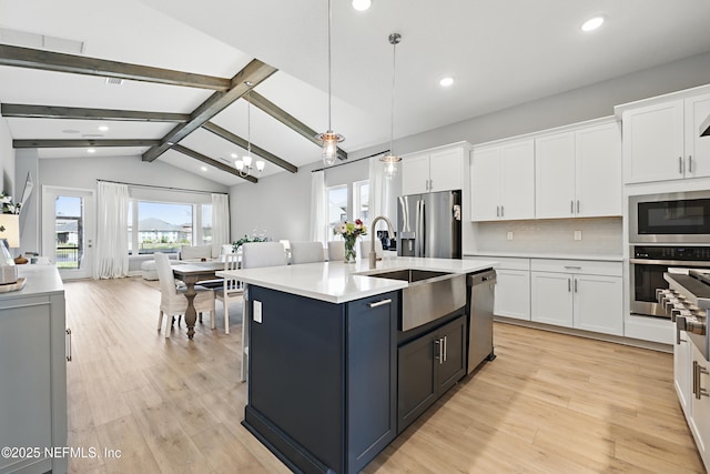 kitchen with a center island with sink, appliances with stainless steel finishes, light countertops, white cabinetry, and pendant lighting