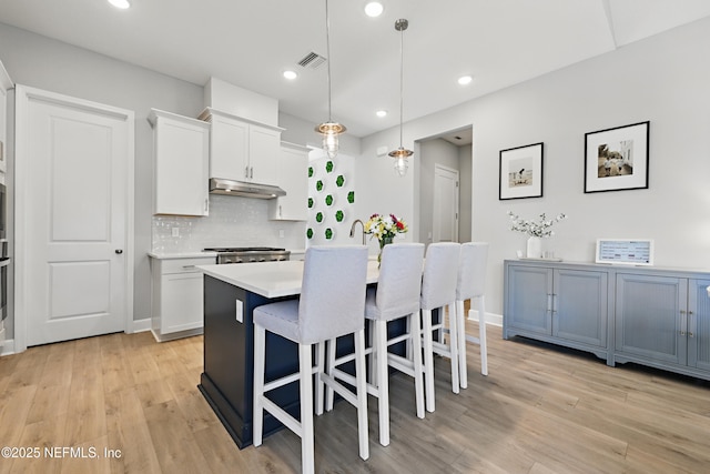 kitchen featuring pendant lighting, light countertops, white cabinetry, an island with sink, and under cabinet range hood