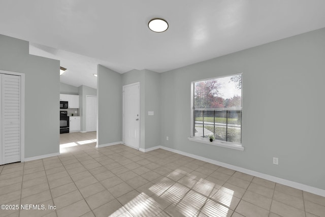 spare room featuring light tile patterned floors, vaulted ceiling, and baseboards