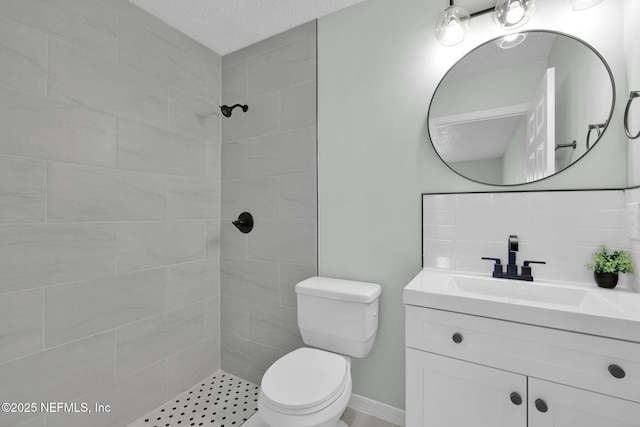 bathroom featuring toilet, tiled shower, a textured ceiling, and vanity