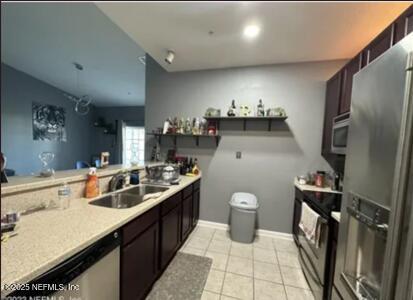 kitchen featuring light tile patterned floors, light countertops, appliances with stainless steel finishes, dark brown cabinetry, and a sink