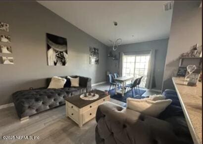 living area featuring vaulted ceiling, light wood finished floors, visible vents, and baseboards