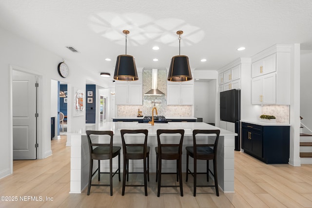 kitchen with light countertops, wall chimney range hood, backsplash, and white cabinetry