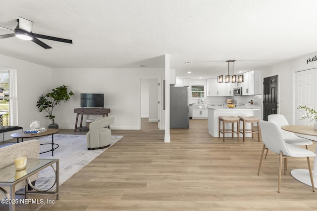 living area featuring light wood-type flooring, a textured ceiling, baseboards, and ceiling fan with notable chandelier