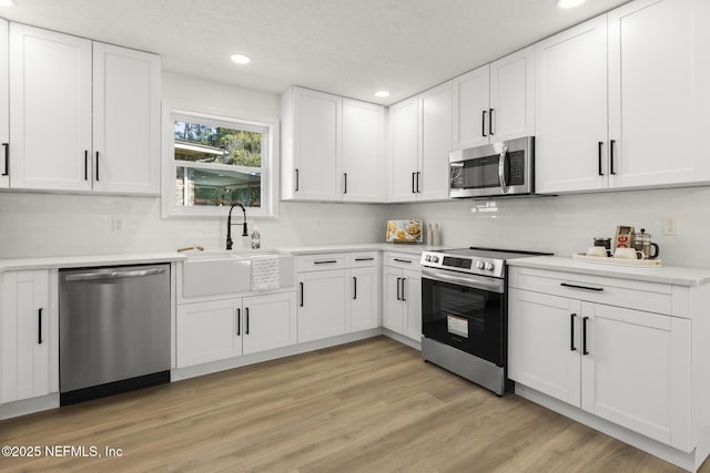 kitchen with stainless steel appliances, light countertops, light wood-style flooring, white cabinetry, and a sink