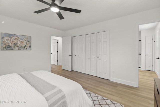 bedroom featuring baseboards, ceiling fan, a textured ceiling, light wood-style floors, and a closet