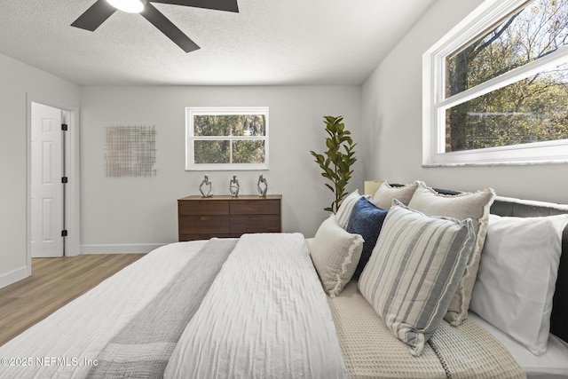 bedroom with a ceiling fan, a textured ceiling, baseboards, and wood finished floors