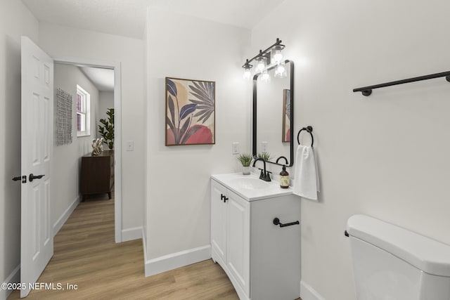 bathroom with toilet, vanity, baseboards, and wood finished floors