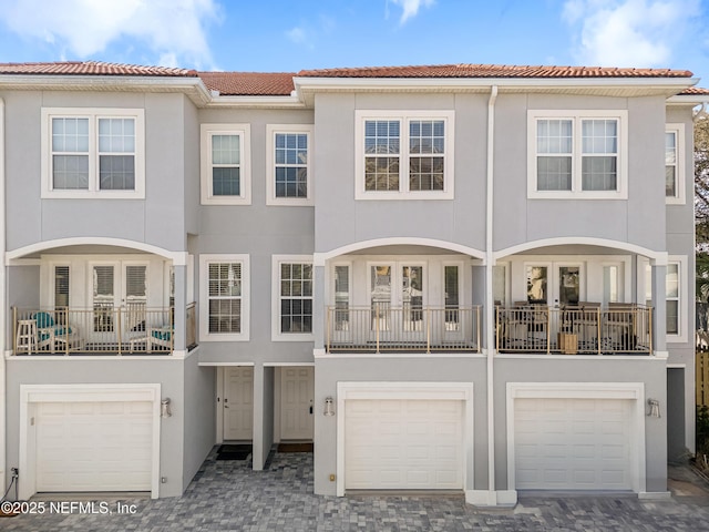 multi unit property with an attached garage, stucco siding, decorative driveway, and a tiled roof