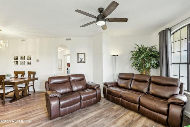 living room featuring baseboards, visible vents, arched walkways, light wood-style floors, and ceiling fan with notable chandelier