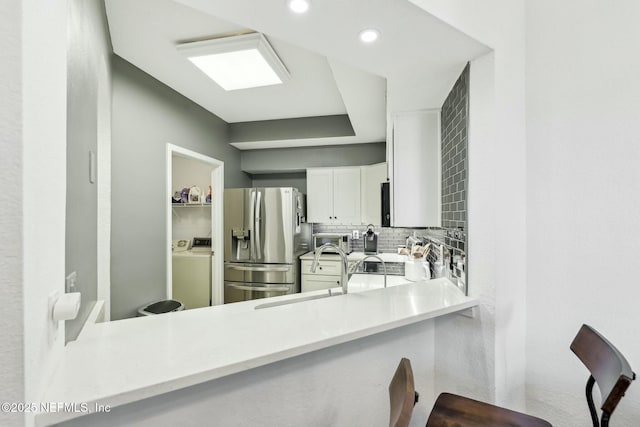 kitchen with white cabinets, decorative backsplash, light countertops, stainless steel refrigerator with ice dispenser, and a sink