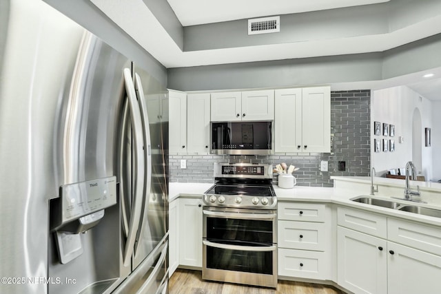 kitchen featuring stainless steel appliances, a sink, white cabinetry, visible vents, and decorative backsplash