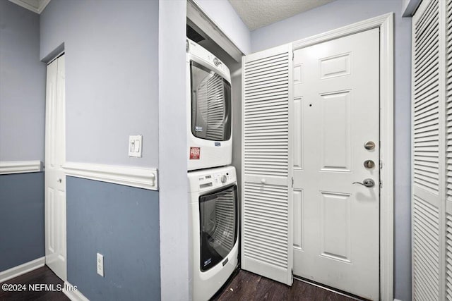 clothes washing area with a textured ceiling, stacked washer and dryer, dark wood-type flooring, laundry area, and baseboards