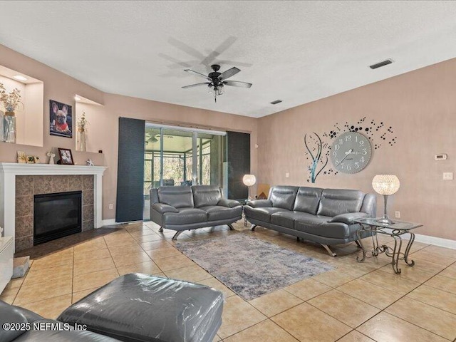 living area with a fireplace, visible vents, a ceiling fan, light tile patterned flooring, and a textured ceiling