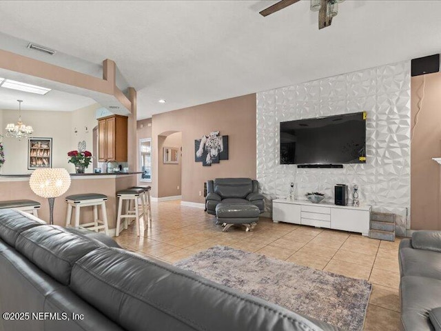 living room featuring light tile patterned floors, baseboards, visible vents, arched walkways, and ceiling fan with notable chandelier