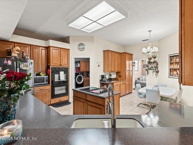 kitchen with washer / dryer, dark countertops, hanging light fixtures, black appliances, and a sink