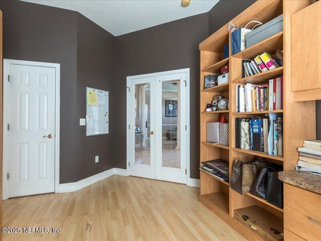 interior space featuring light wood-type flooring, baseboards, a textured ceiling, and french doors