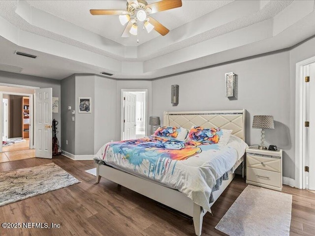 bedroom featuring baseboards, visible vents, a ceiling fan, dark wood-style floors, and a tray ceiling