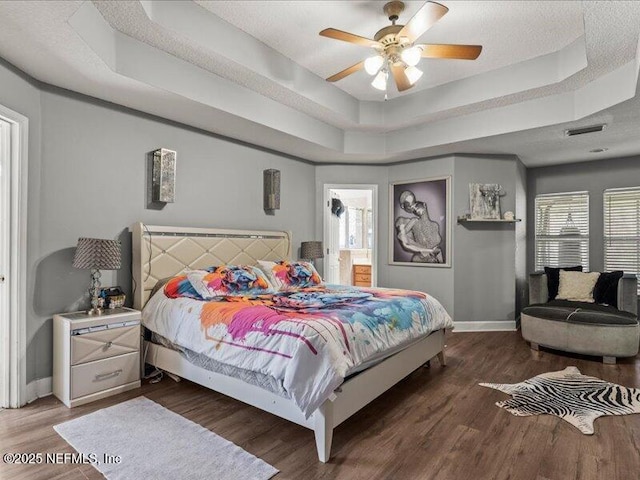 bedroom with a tray ceiling, dark wood-style flooring, visible vents, and baseboards