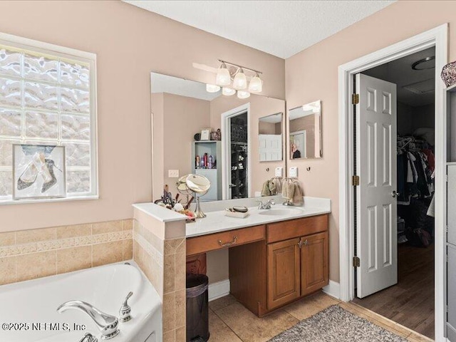 full bathroom featuring a walk in closet, a garden tub, vanity, and tile patterned floors