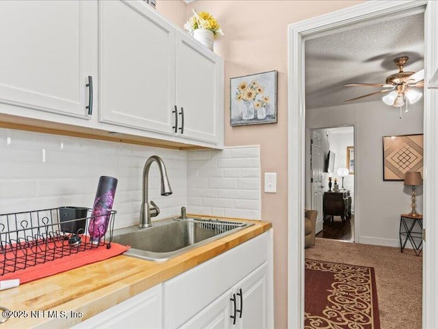 kitchen featuring carpet floors, backsplash, a ceiling fan, white cabinetry, and a sink