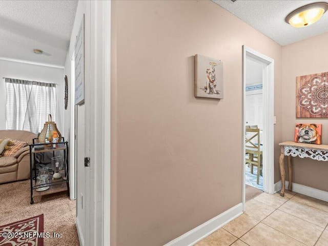 hallway featuring a textured ceiling, light tile patterned floors, and baseboards