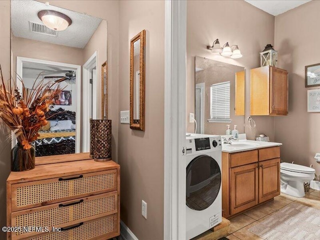 bathroom with toilet, visible vents, vanity, baseboards, and washer / dryer