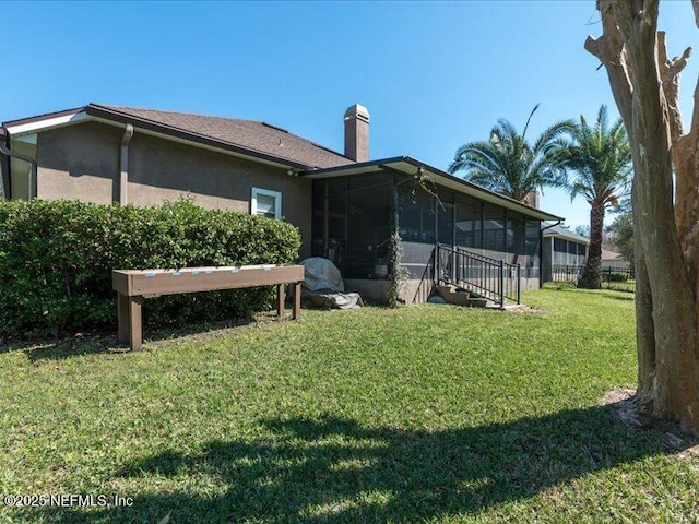 rear view of property featuring a sunroom, a lawn, a chimney, and stucco siding