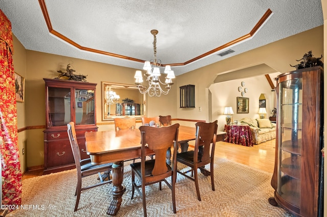 dining space featuring a chandelier, a tray ceiling, wood finished floors, and visible vents