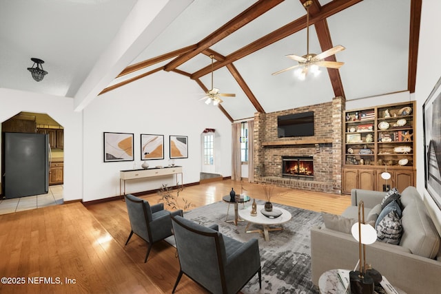 living room with high vaulted ceiling, a fireplace, light wood-style flooring, and beamed ceiling