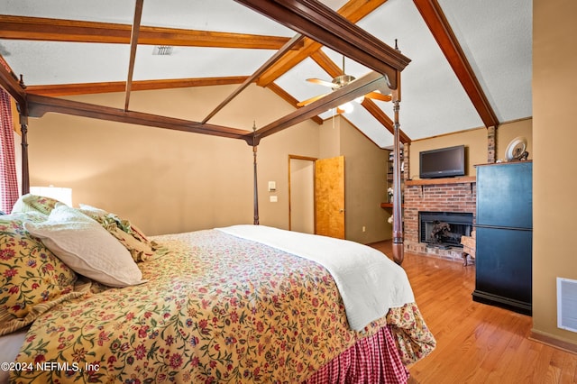 bedroom featuring refrigerator, visible vents, light wood-style flooring, lofted ceiling with beams, and a brick fireplace