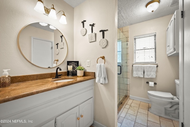 bathroom with stone tile flooring, a textured ceiling, a shower stall, vanity, and baseboards