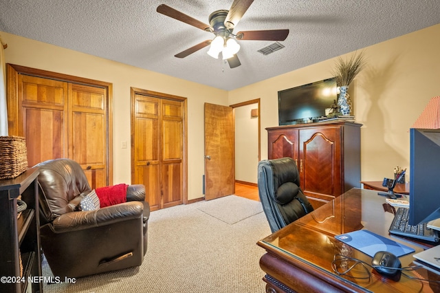 office space featuring a ceiling fan, visible vents, light carpet, and a textured ceiling