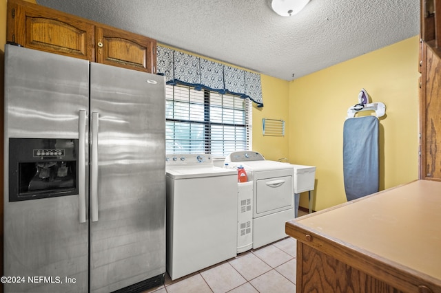 clothes washing area with washing machine and dryer, a sink, a textured ceiling, and light tile patterned floors