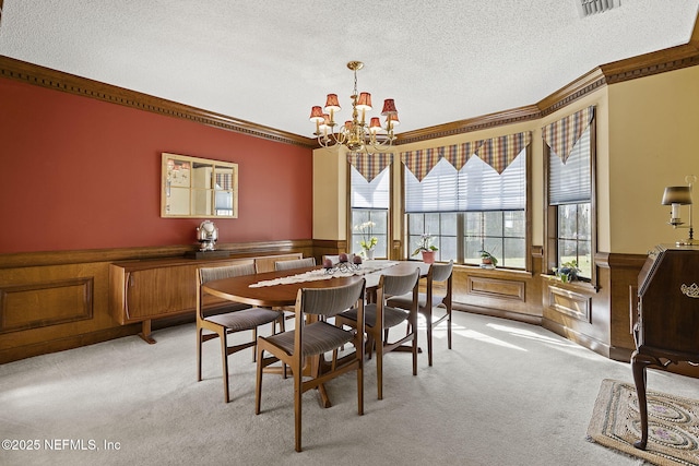 dining room featuring light carpet, crown molding, a textured ceiling, and wainscoting