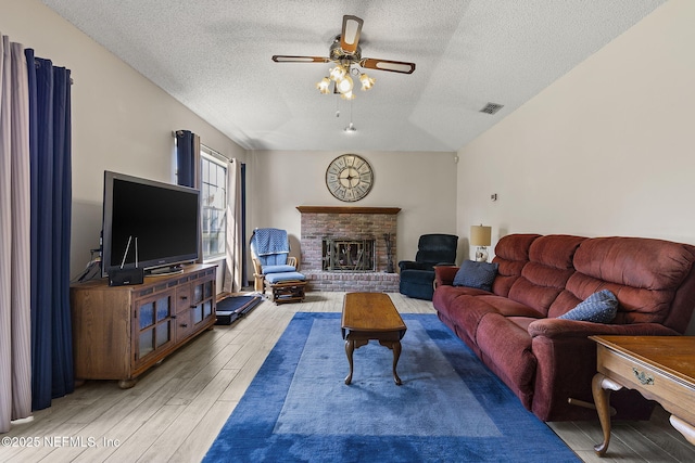 living area featuring visible vents, a brick fireplace, ceiling fan, a textured ceiling, and wood finished floors